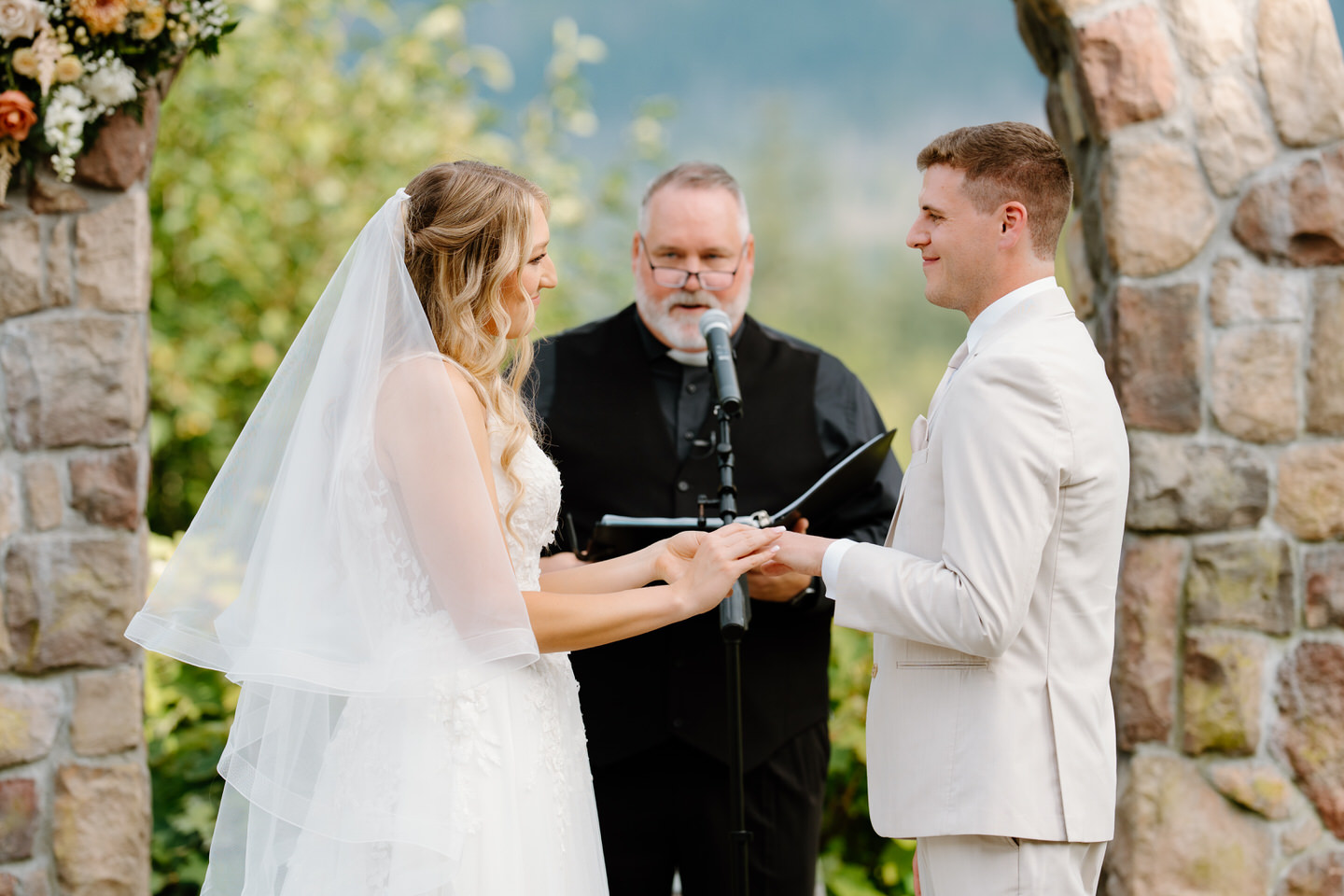 Bride and groom exchange rings, with their officiant reading behind them.