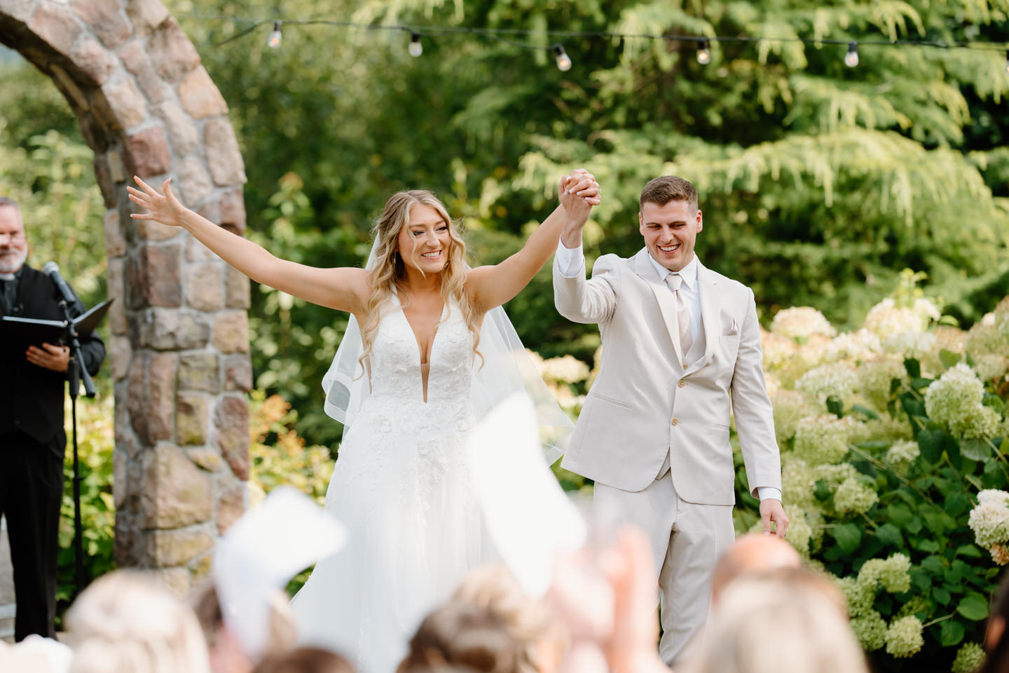 Bride and groom raise their arms with cheer at Cape Horn Estate garden.