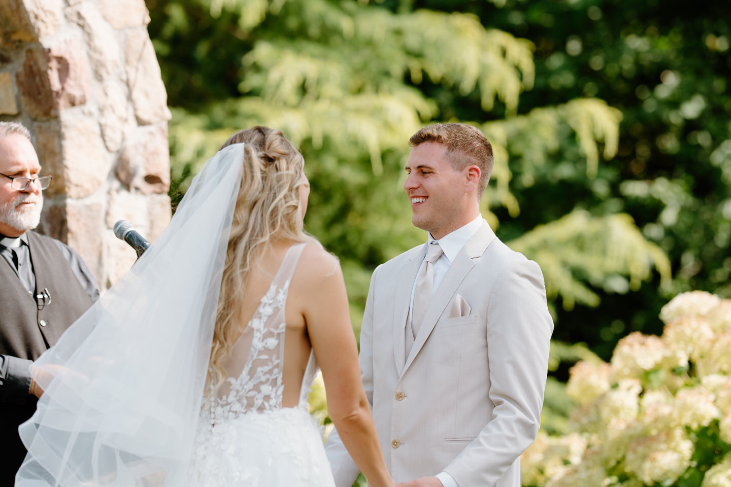Groom holding his bride's hands and smiling in front of the stone altar.