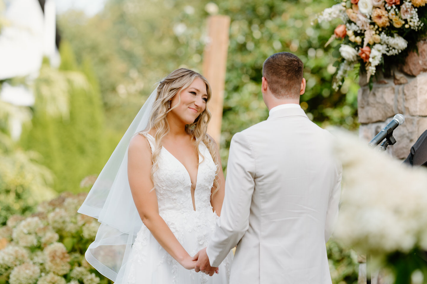 Bride smiles at the groom as they hold hands during wedding ceremony.