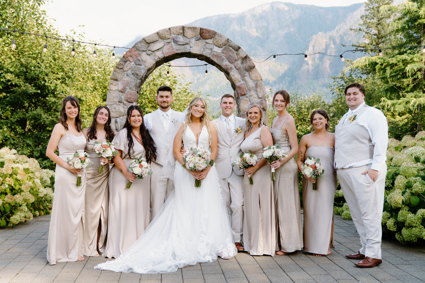 The entire wedding party smiling in front of the stone arch at Cape Horn Estate.