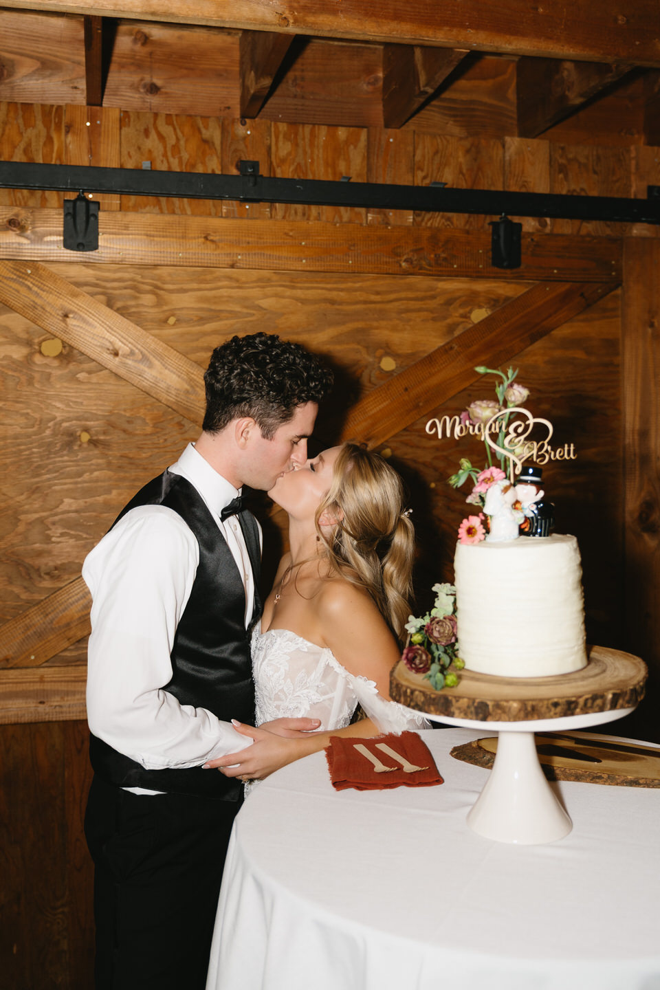 Couple kiss next to their wedding cake.