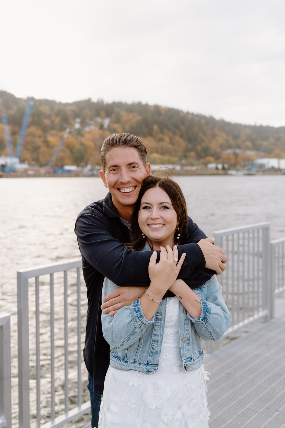 Man wraps his arms around his bride-to-be on a fall Portland day at Cathedral Park.