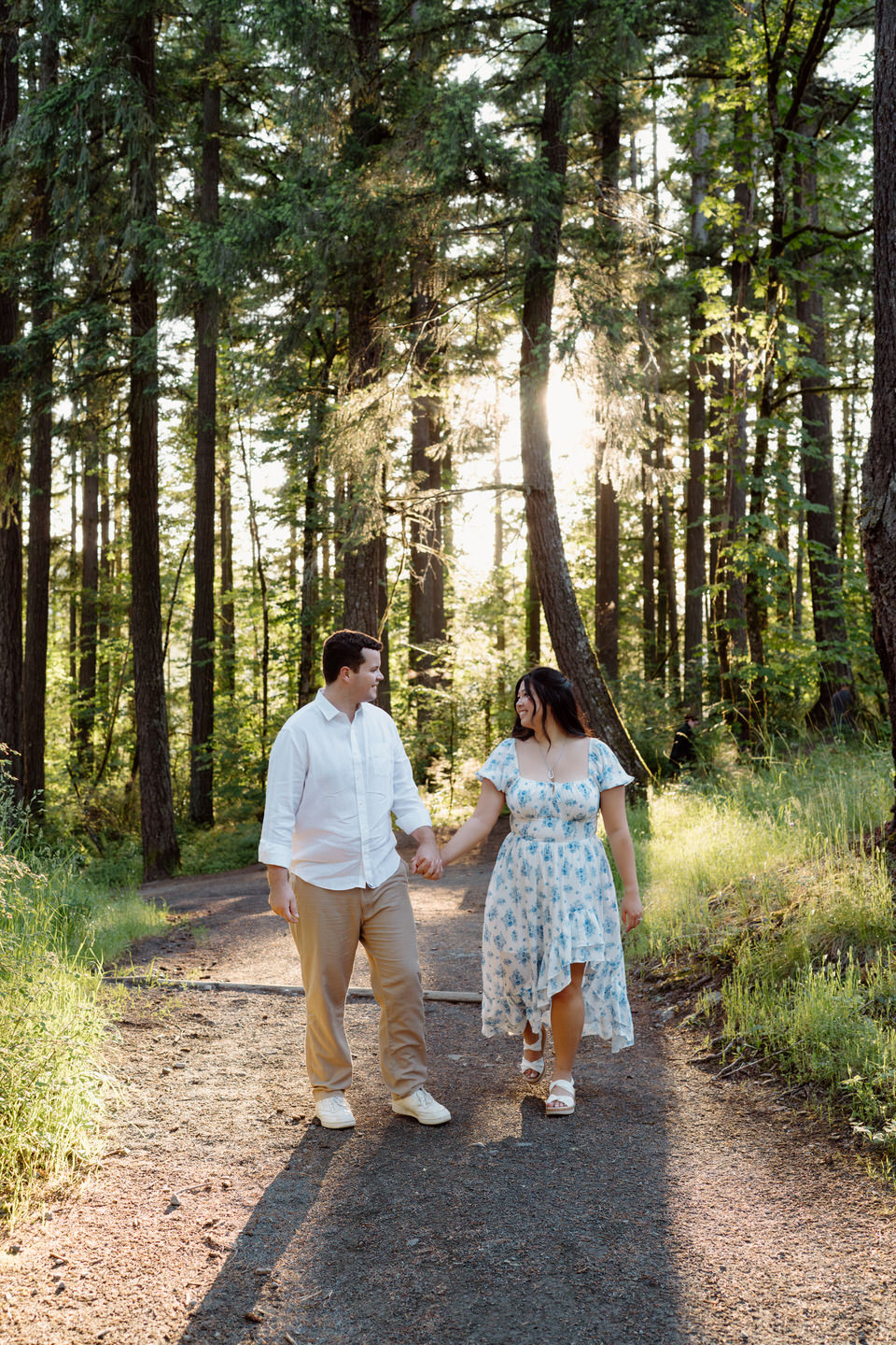 They stroll hand in hand down a dirt path, surrounded by tall pines and glowing light in this Vancouver, WA Engagement session.