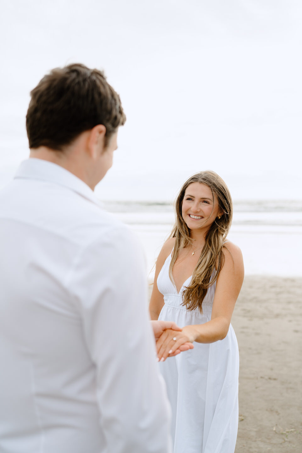 Man holds his fiancee's ring hand, looking out at the ocean.