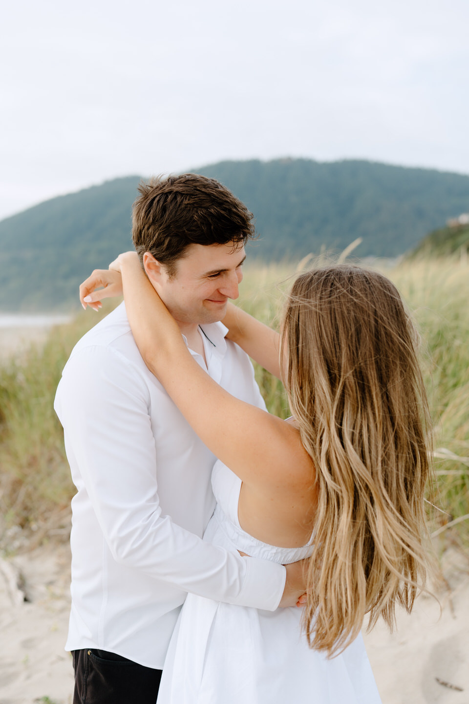 Couple hanging on to each other, looking into each other's eyes lovingly, among the beach grass in Manzanita.