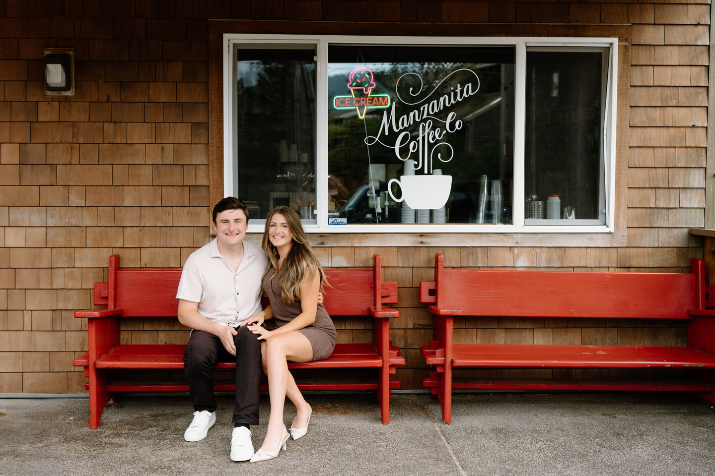 Couple in formal attire sitting on a red bench in front of Manzanita Coffee Co window.