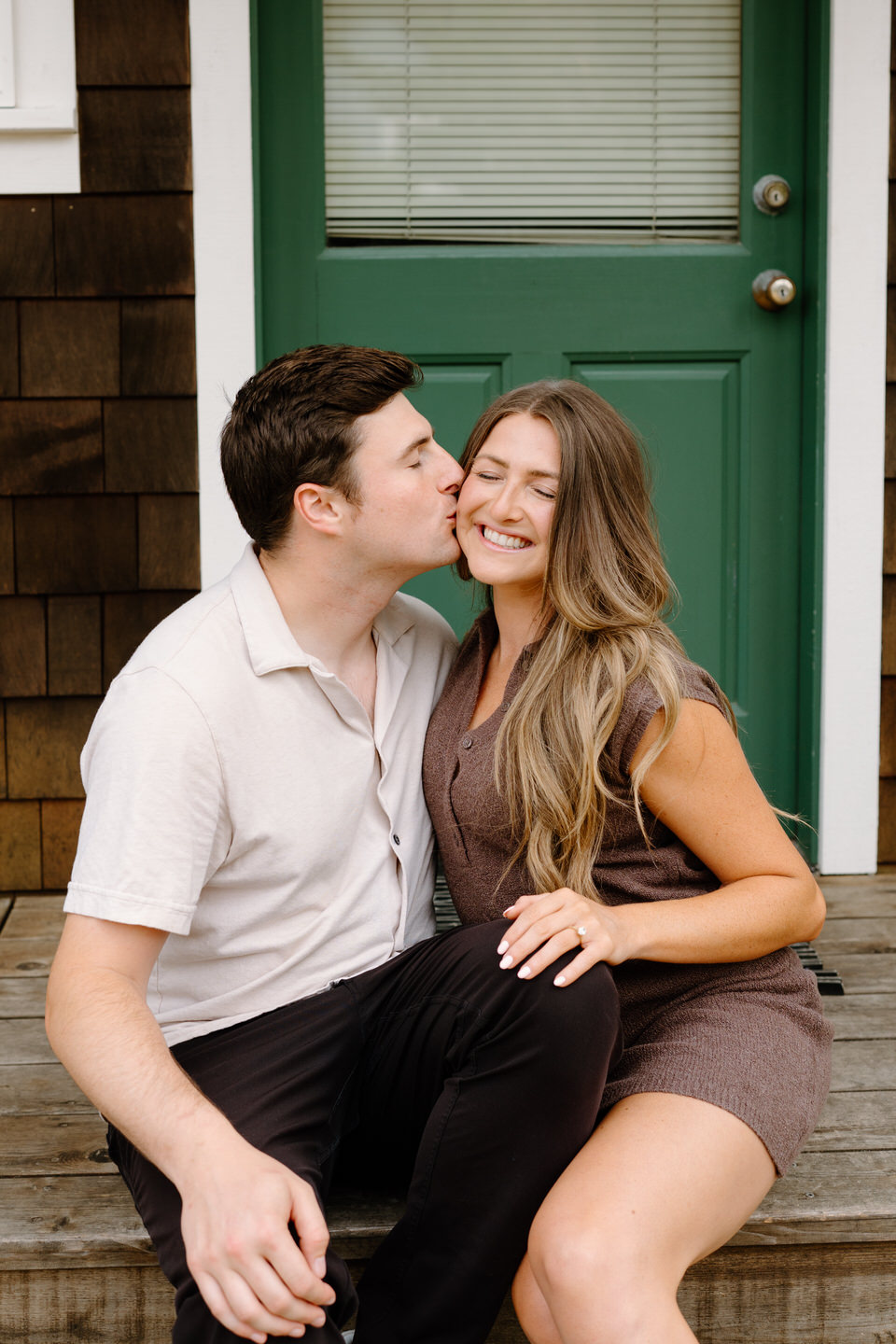 Couple sitting on front porch, man kissing woman on the cheek.