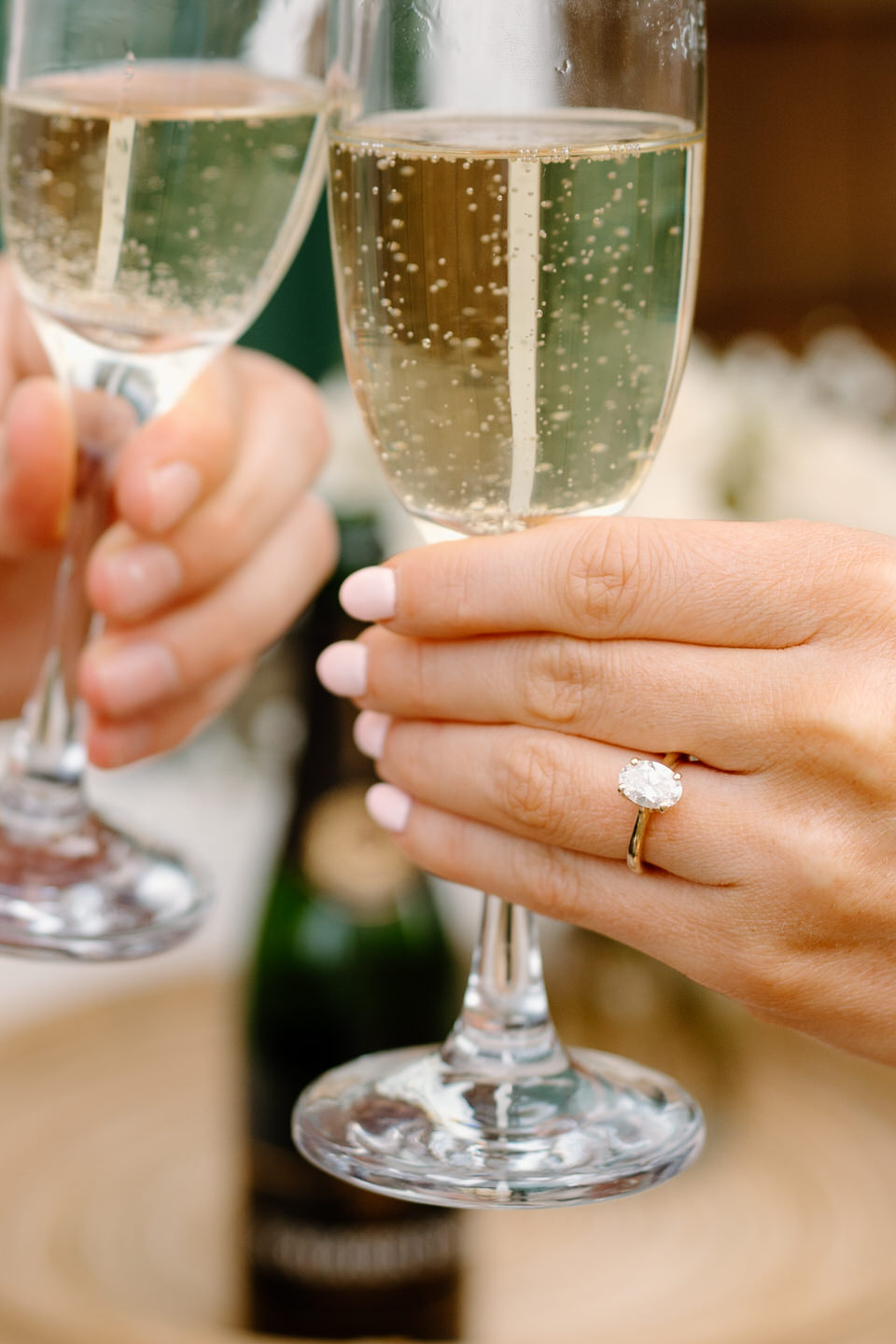 Close up on oval engagement ring, holding a champagne glass.