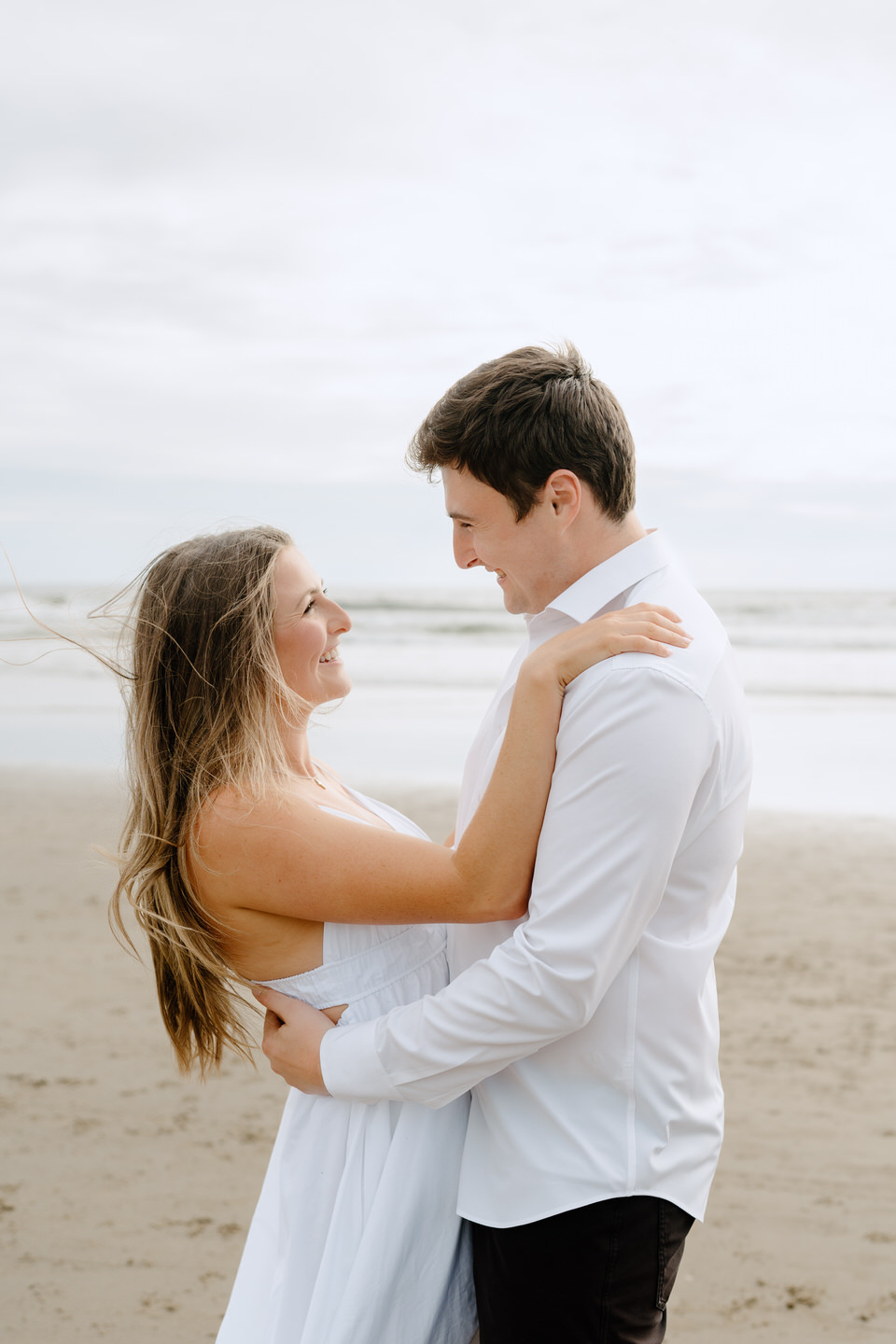 Couple wraps their arms around each other on the beach with dreamy lighting.