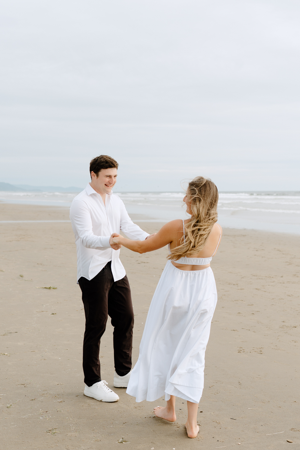 Engaged couple holds hands and spins around during Manzanita engagement photos.