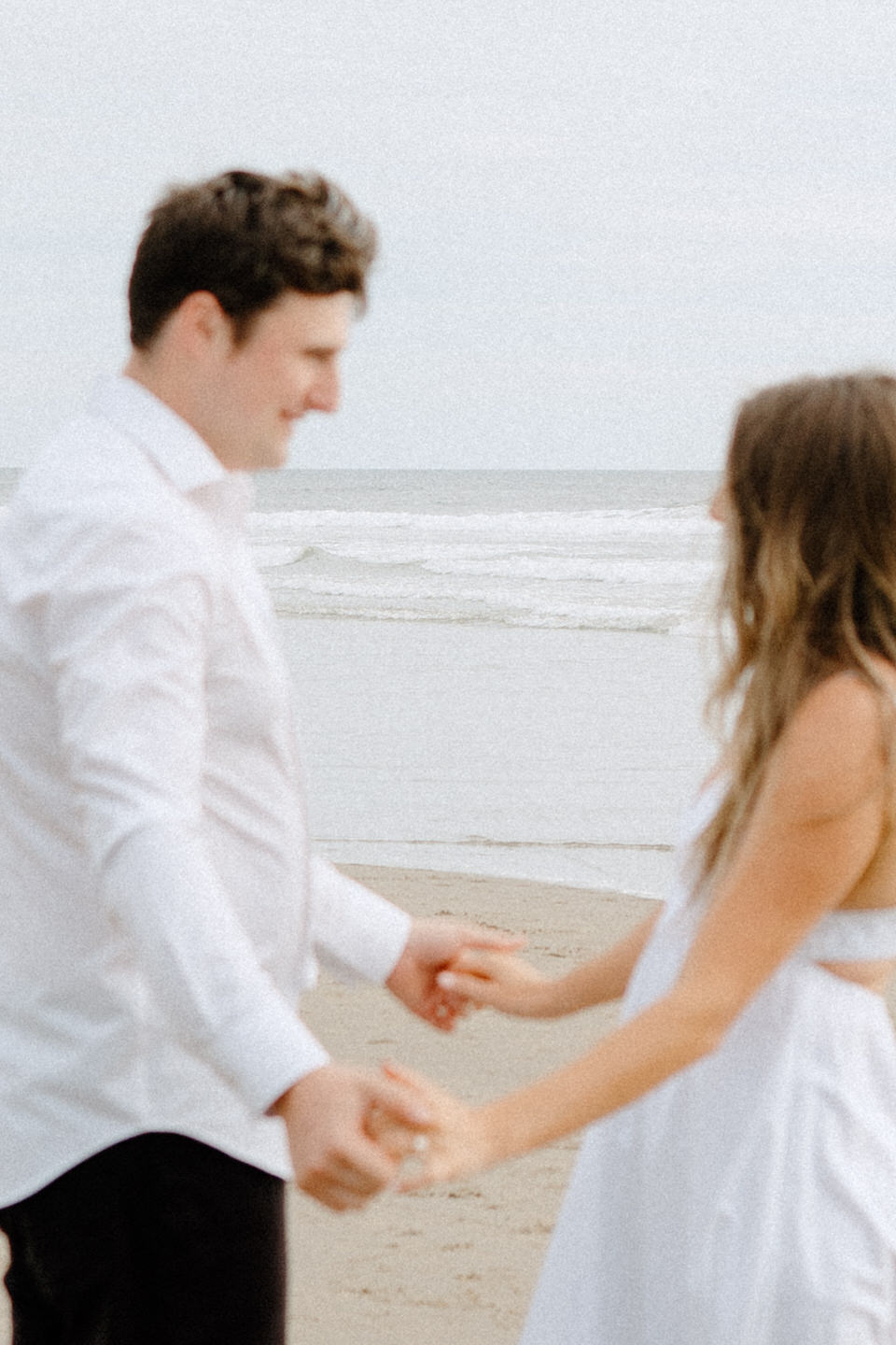 Close up of couple holding hands with waves in the background.