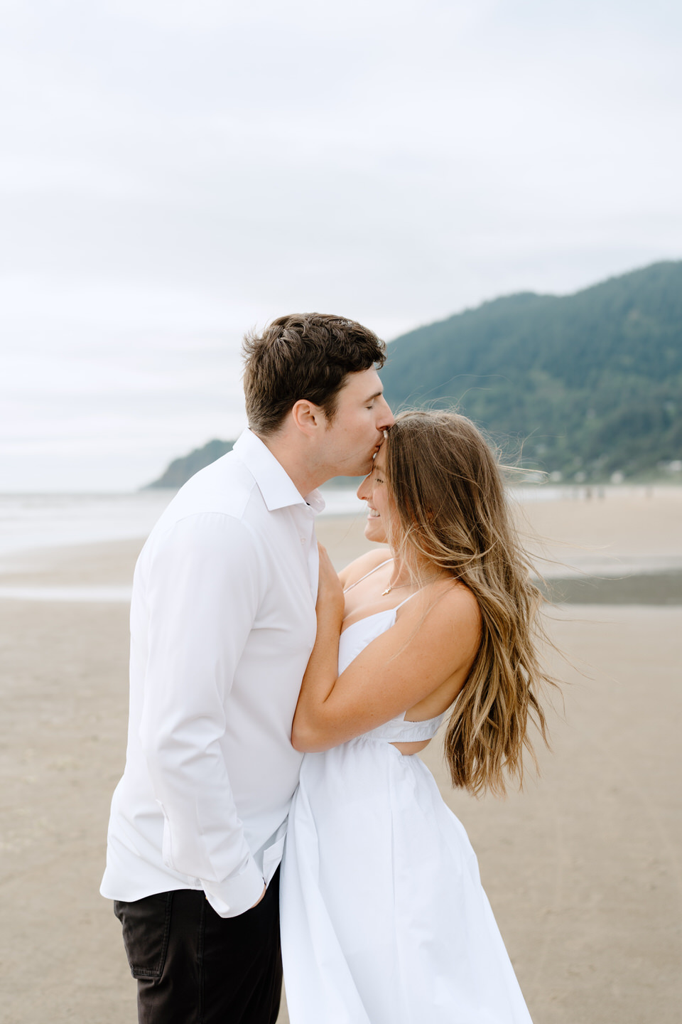 Man kisses woman on the forehead during Manzanita engagement photos.