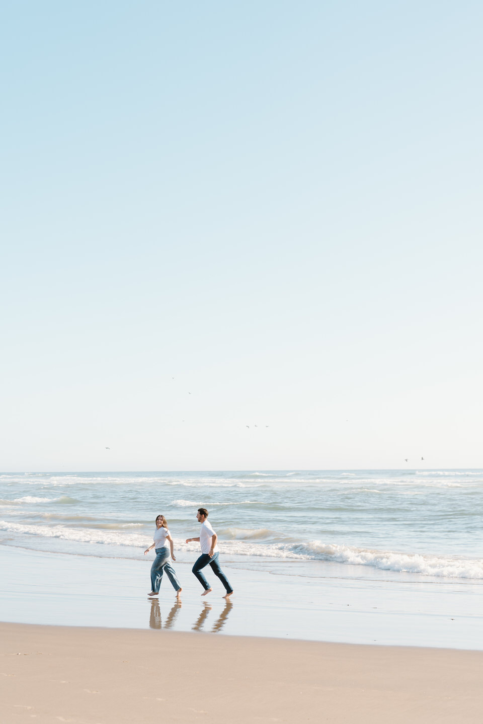 Couple runs playfully along the water at Cannon Beach.