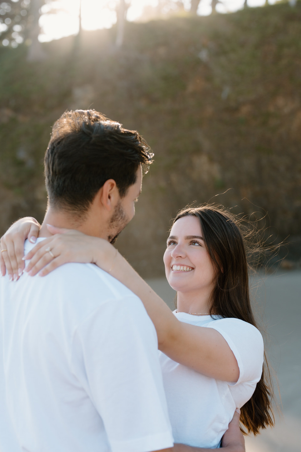 Woman wraps her arms around her fiancé's shoulders, showing off her engagement ring with the Oregon coast cliffs in the background.