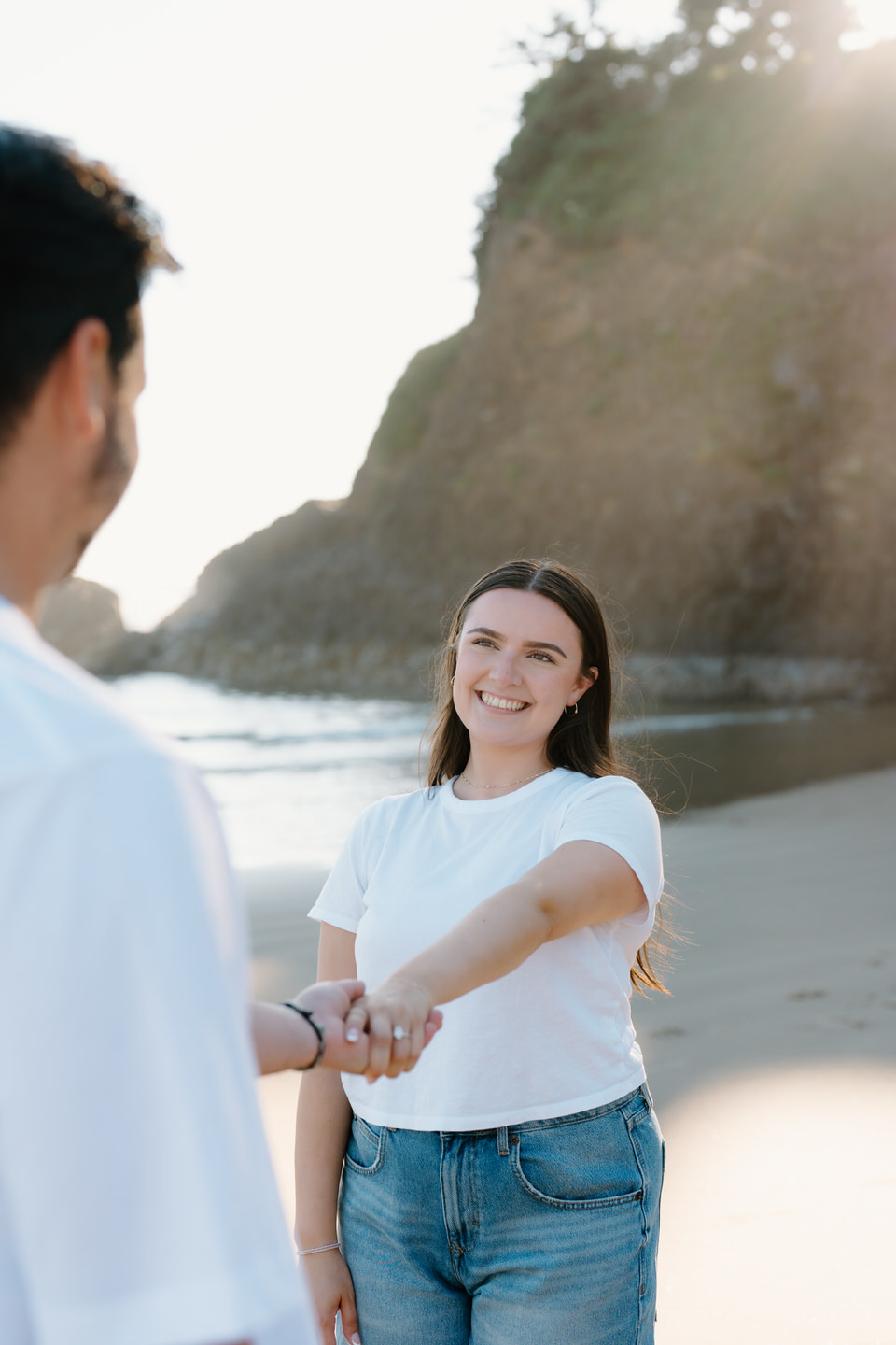 Woman extends her hand out towards her fiancé, beaming at him. 