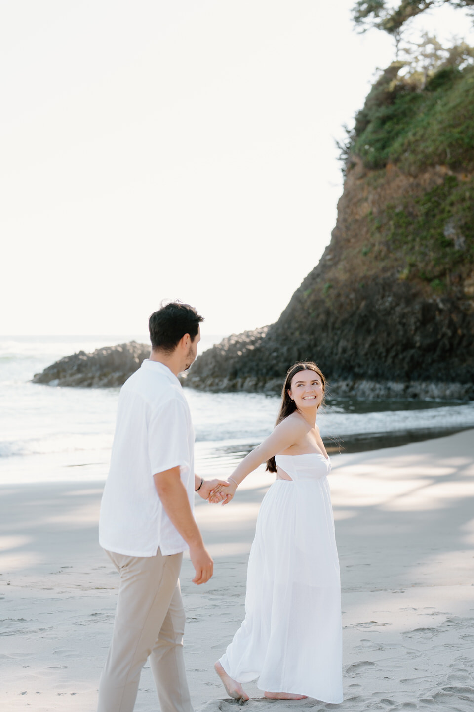 Woman looks back at man as they take dreamy engagement photos on the Oregon coast.