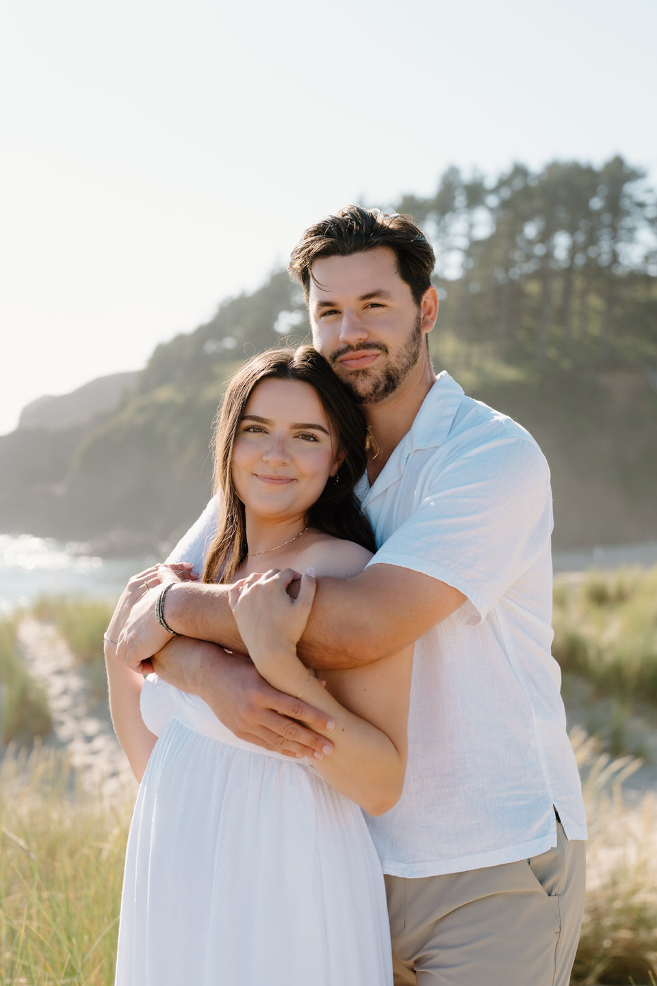 Couple gives soft smiles to the camera, surrounded by dreamy landscapes and seagrass.
