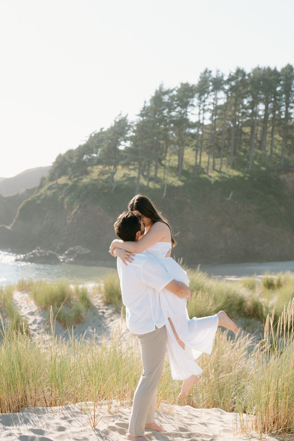 Man picks up woman and spins her around in the sand.