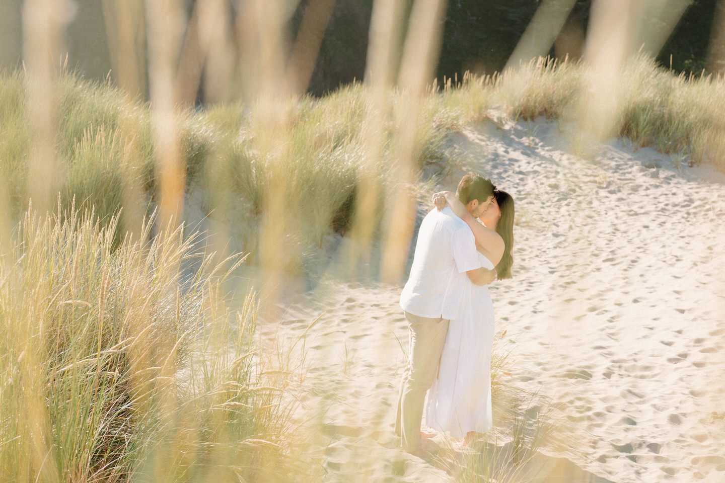Photo taken through seagrass, with couple kissing in the background.