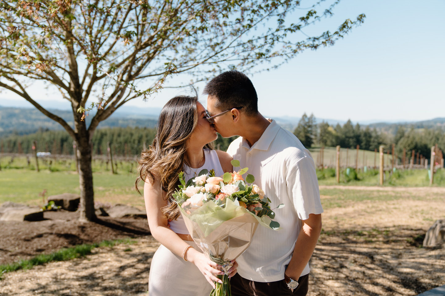 Couple sharing a kiss among vineyard rows at Eminent Domaine winery with rolling hills behind them.