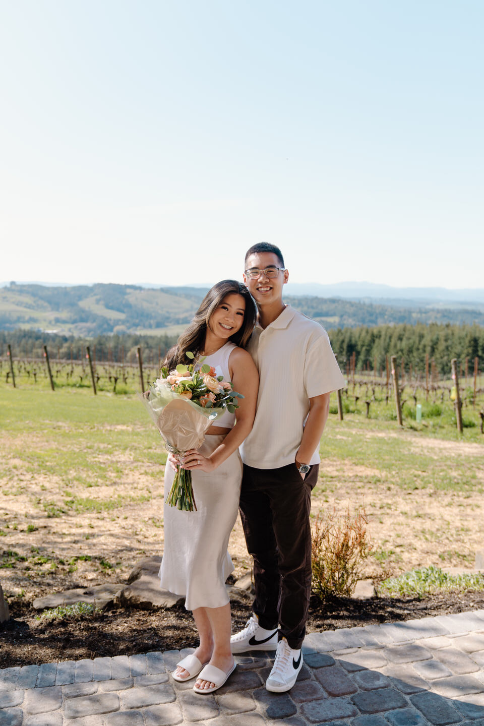 Engaged couple celebrating with a bouquet in the vineyards at Eminent Domaine winery in April.