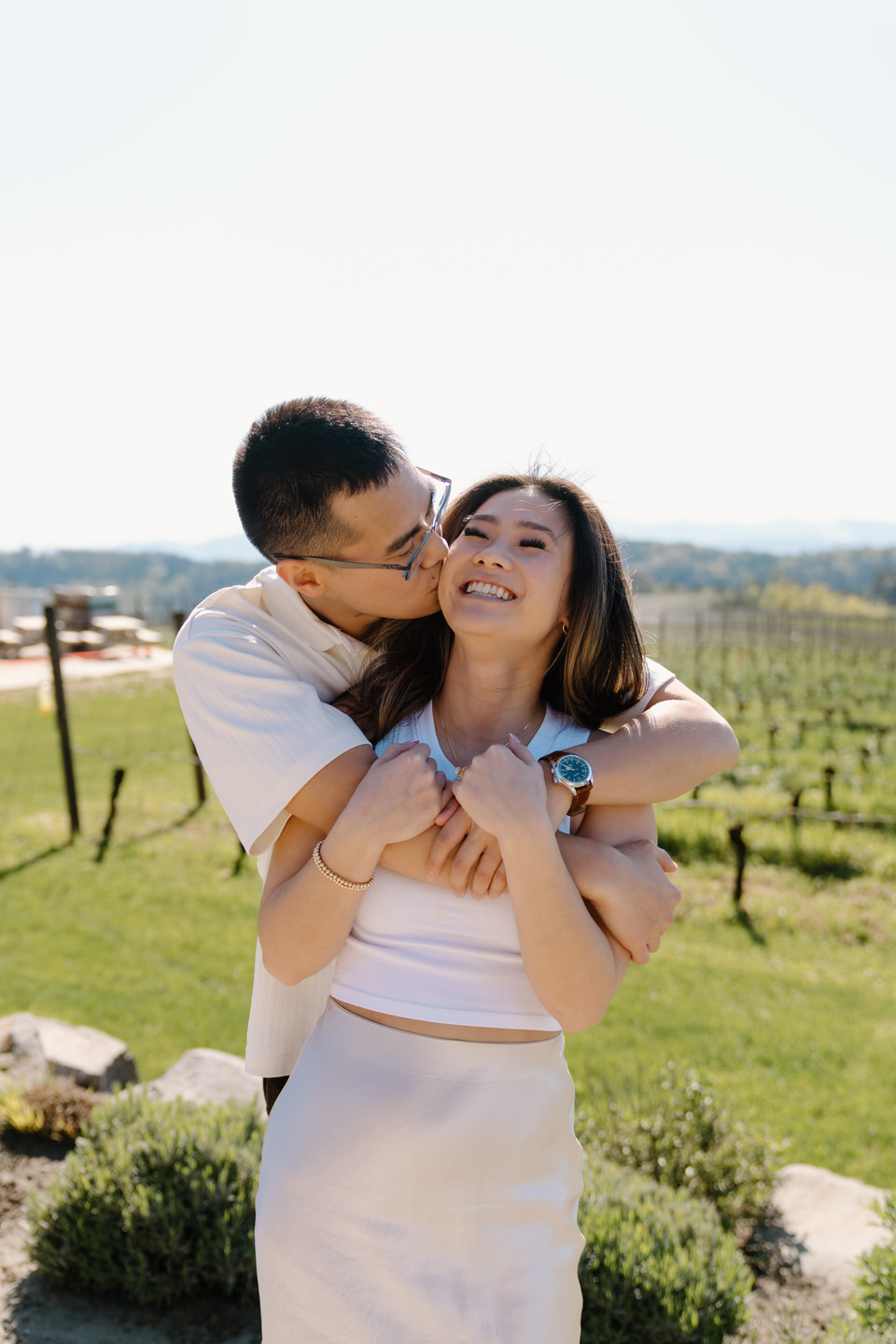 Oregon wine country proposal at Eminent Domaine with couple cuddling among lush green vines in April.