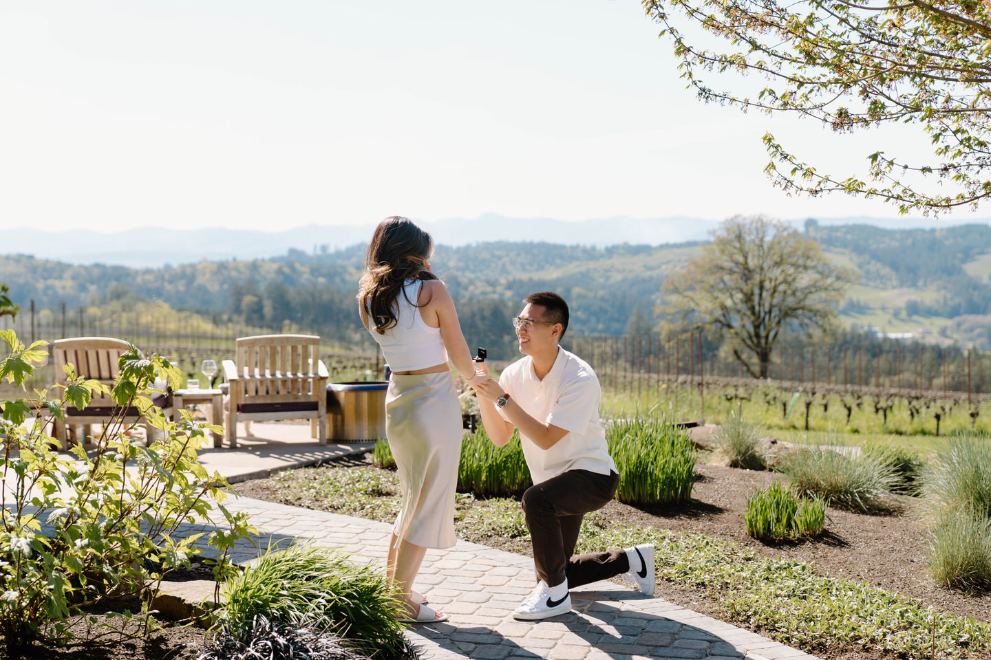 Man proposes to his girlfriend on one knee in front of the Oregon wine country vineyard.