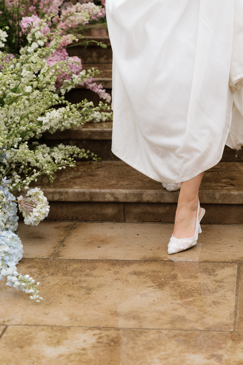 Close-up of the bride’s heels stepping down stone stairs, highlighting delicate details and classic bridal style.