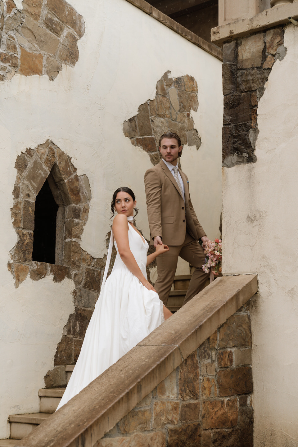 The couple stands in a stone corridor holding hands, showcasing timeless architecture at chateau de lis.