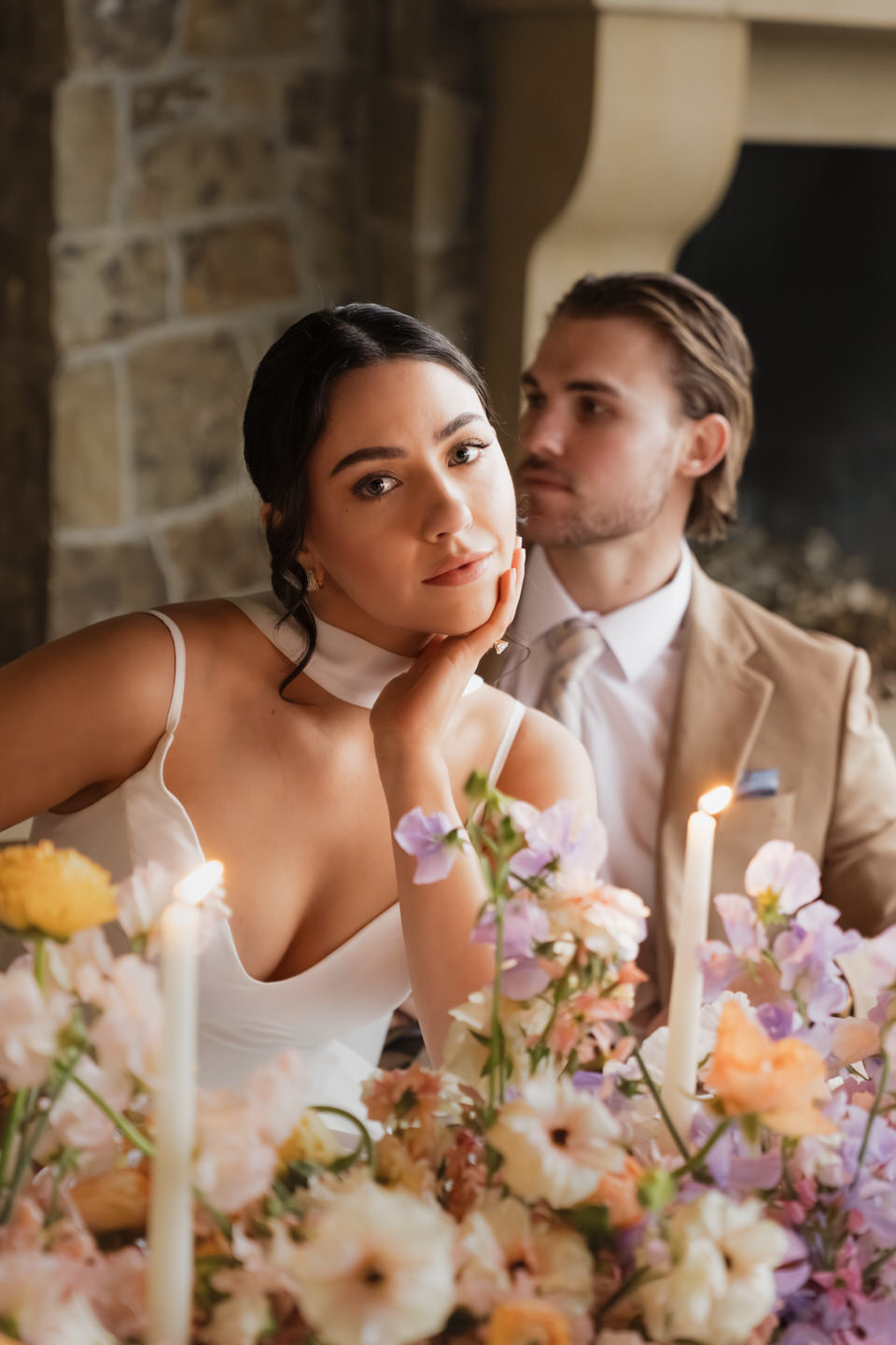 Bride gazes toward the camera as the groom kisses her cheek, surrounded by warm stone walls at chateau de lis.