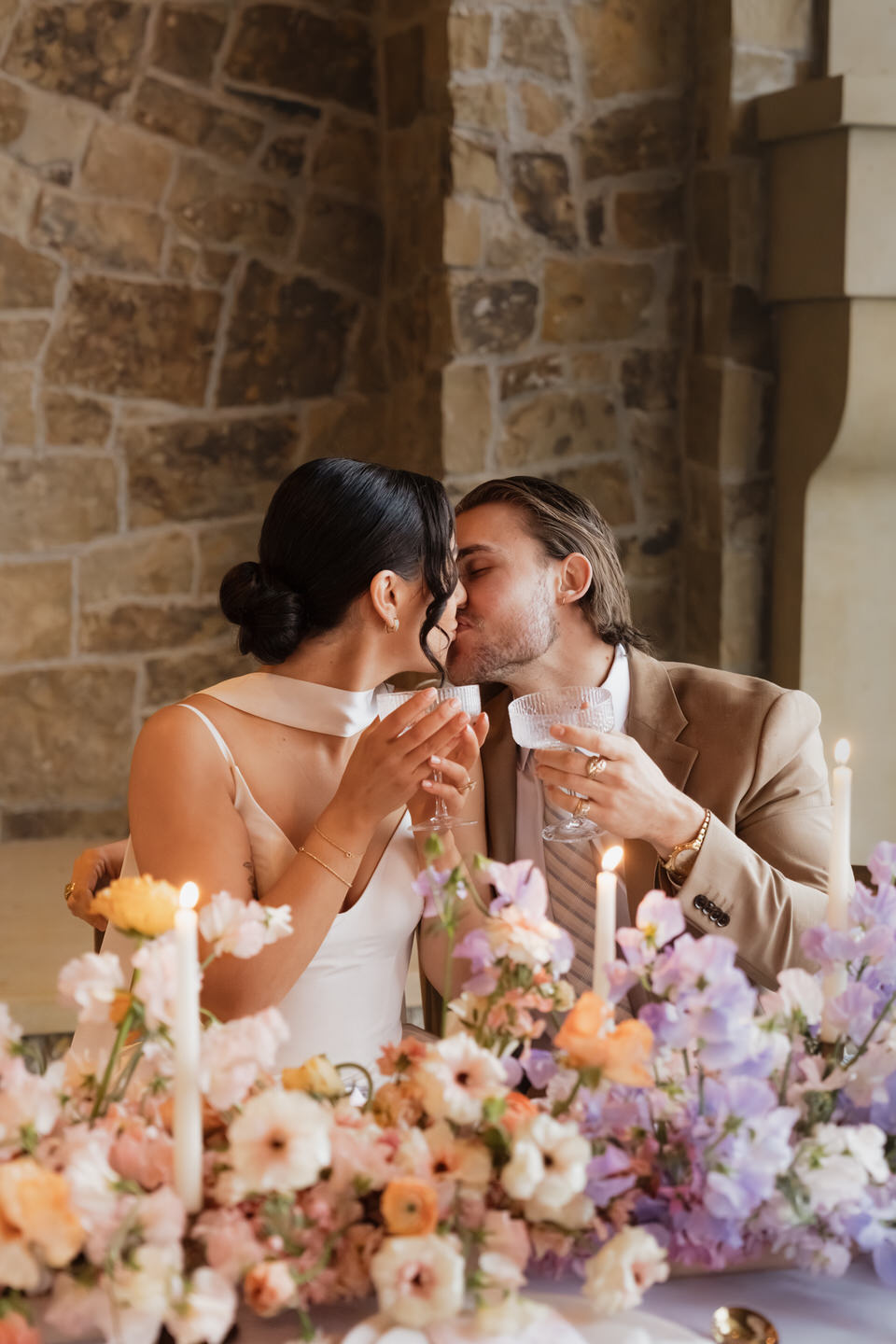 The couple laughs together at a floral-filled reception table, candles glowing softly at chateau de lis.