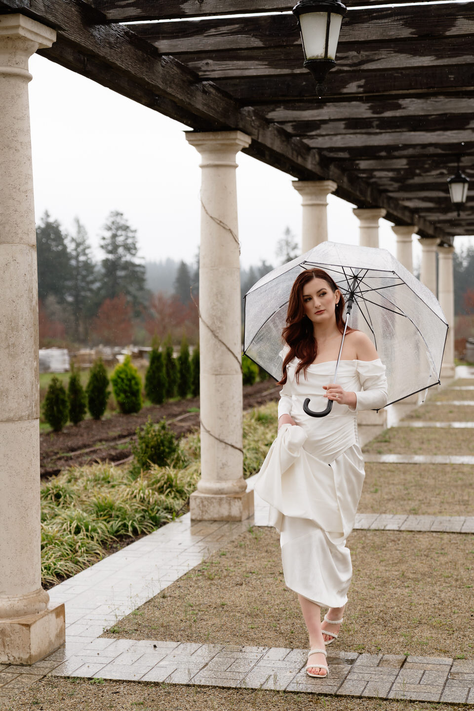 Bride walks through the European-style outdoor venue in the rain with her umbrella.