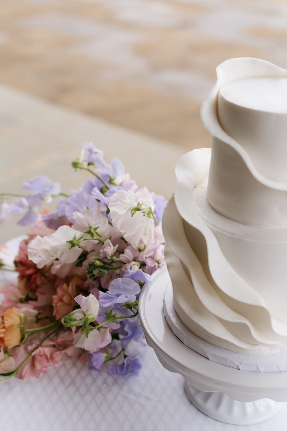 Textured wedding cake with cascading florals styled against soft neutral tones.