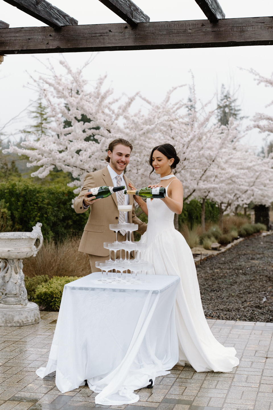 Couple pouring a champagne tower in the cherry blossoms at Chateau de Lis. 