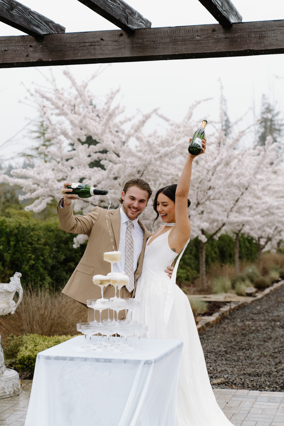 Bride and groom celebrate over a champagne tower in the cherry blossoms at Chateau de Lis.