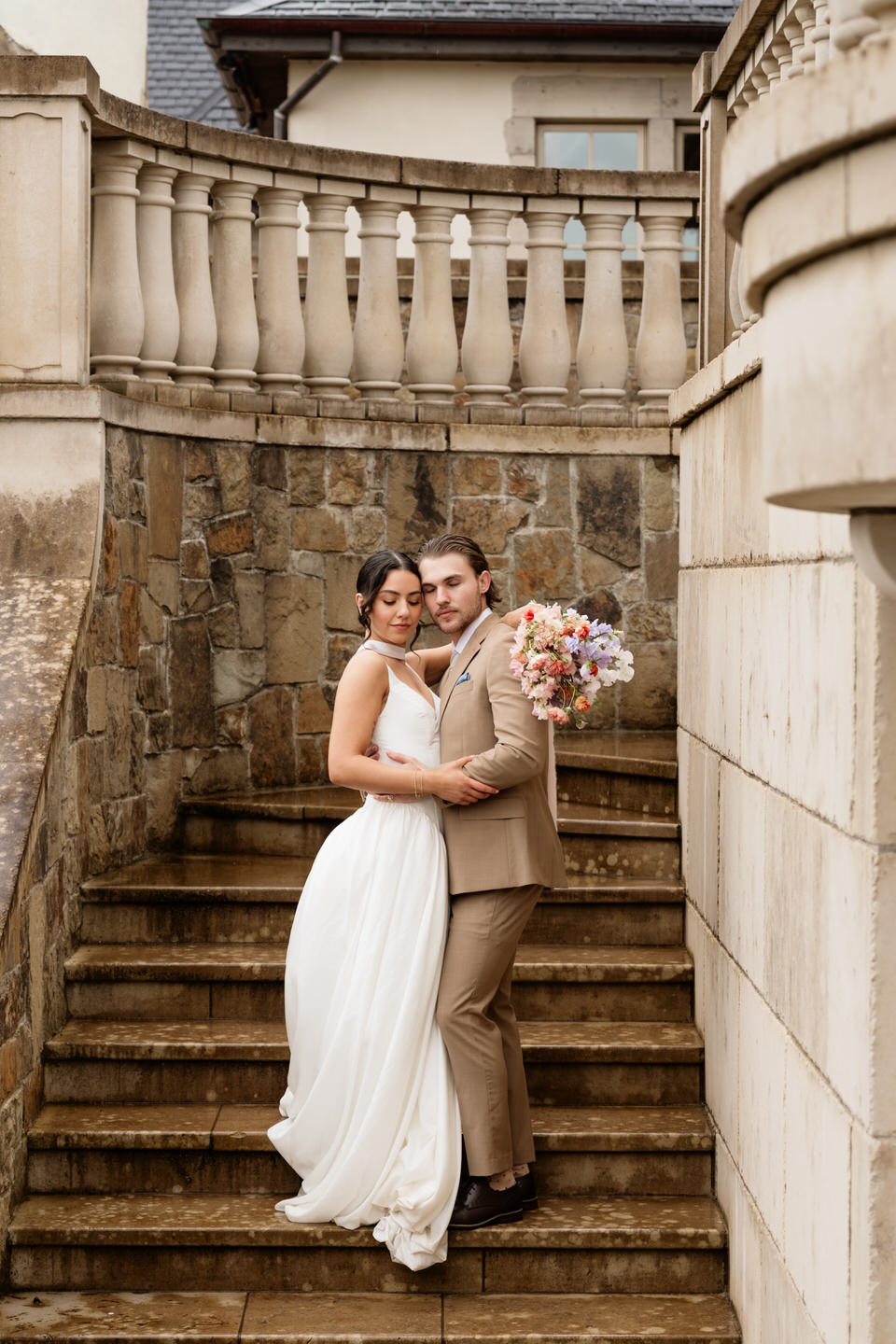 The couple holds a colorful bouquet together, framed by stone staircases at chateau de lis.