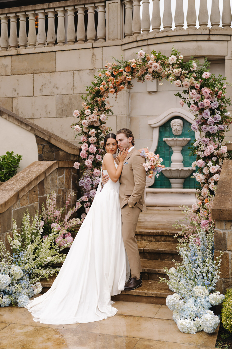 The couple holds each other beneath the floral arch, showcasing timeless wedding elegance and balance.