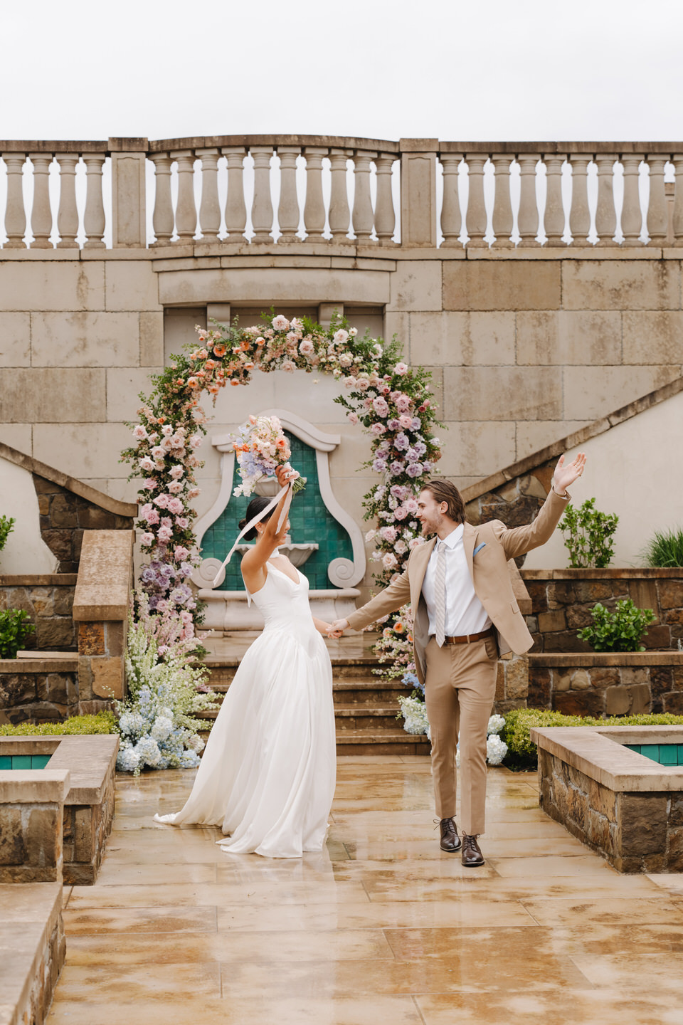 The couple dances together beneath a grand floral installation, celebrating joy in an elegant outdoor space.