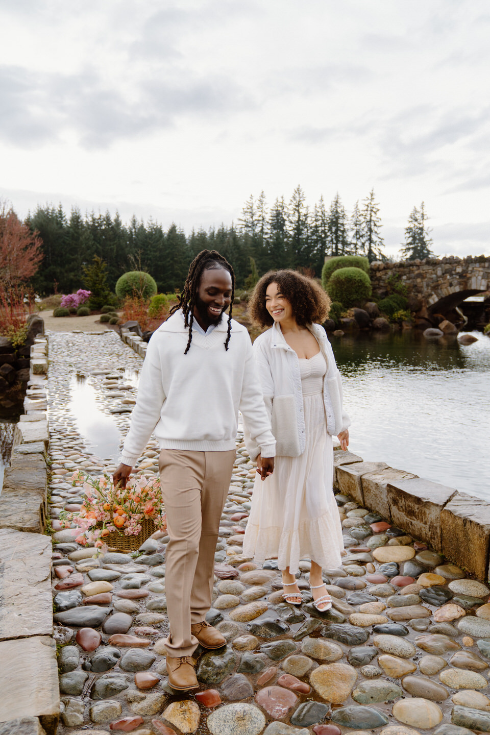 Strolling across stone path at Chateau de Lis with couple holding hands beside reflective water and greenery.