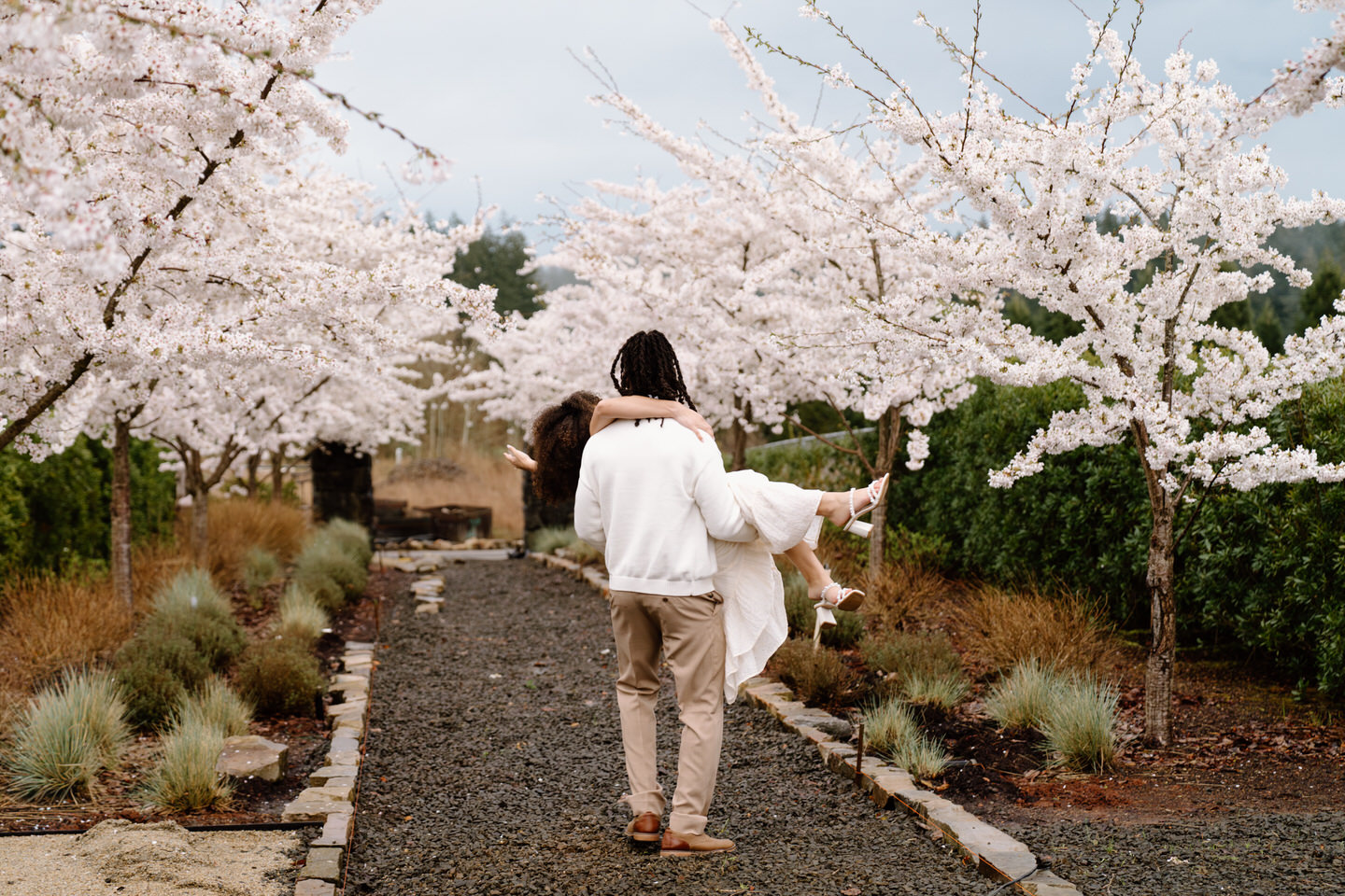 Couple walking away hand in hand under flowering trees at Chateau de Lis during a romantic engagement session.