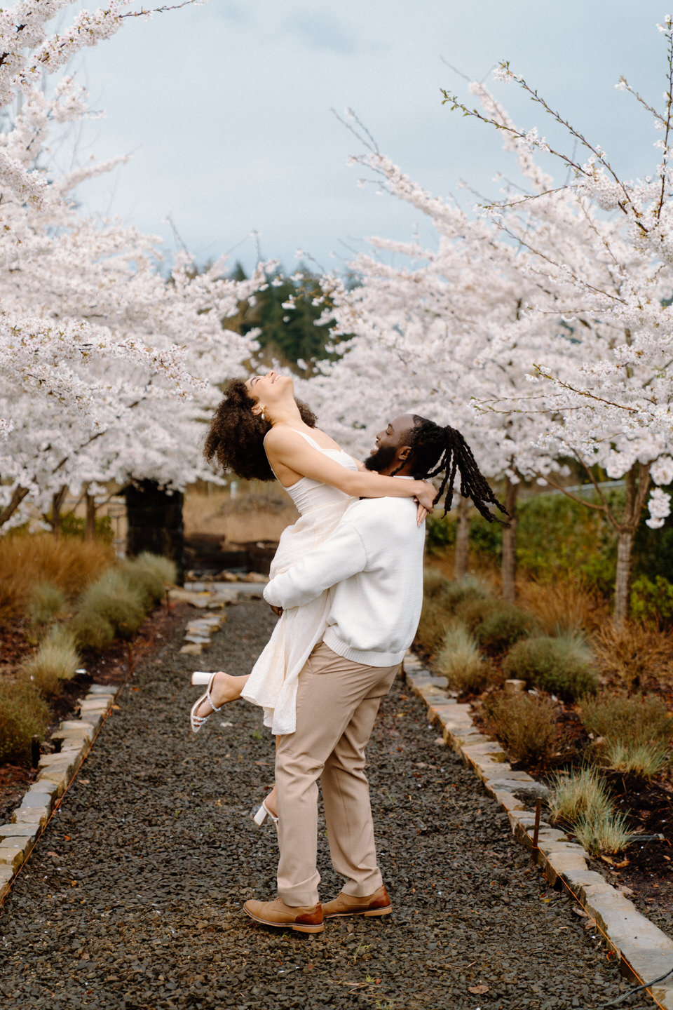Couple laughing as he lifts her under flowering trees at Chateau de Lis, capturing movement and joy.