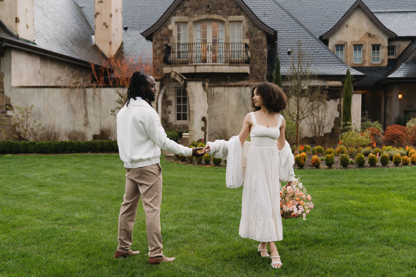 Couple holding hands on the lawn at Chateau de Lis, framed by stone architecture and soft spring light.