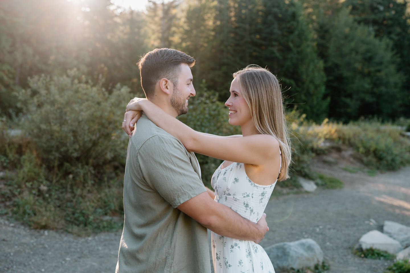 Couple holding each other closely with warm sunlight filtering through trees during engagement photos at Trillium Lake.