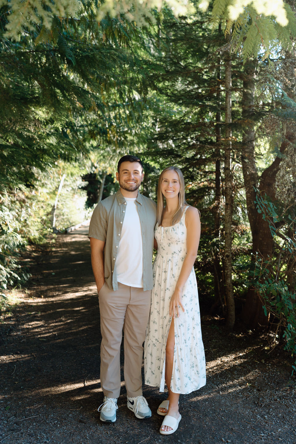 Couple standing side by side in the woods with summer formal outfits.