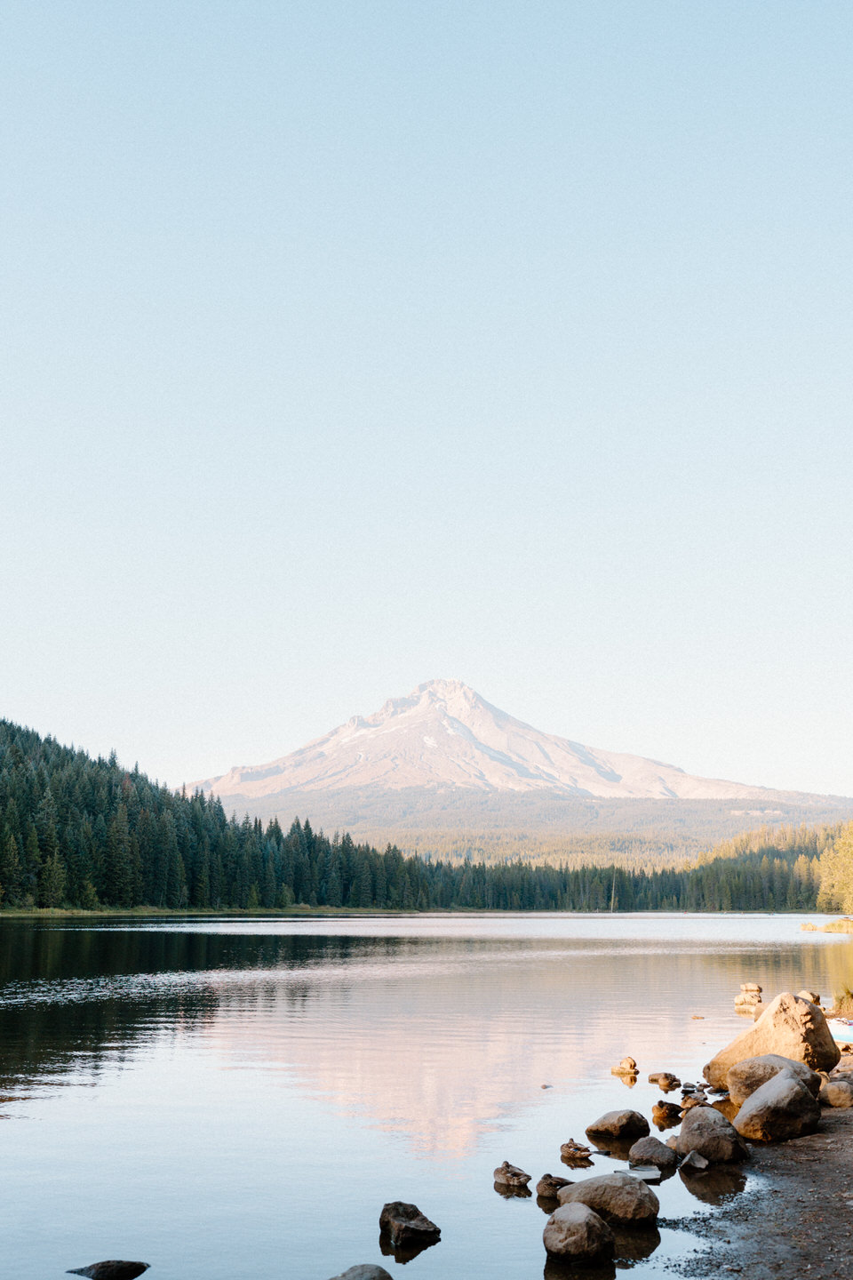 Wide scenic view of Mount Hood and calm lake water surrounded by forest.