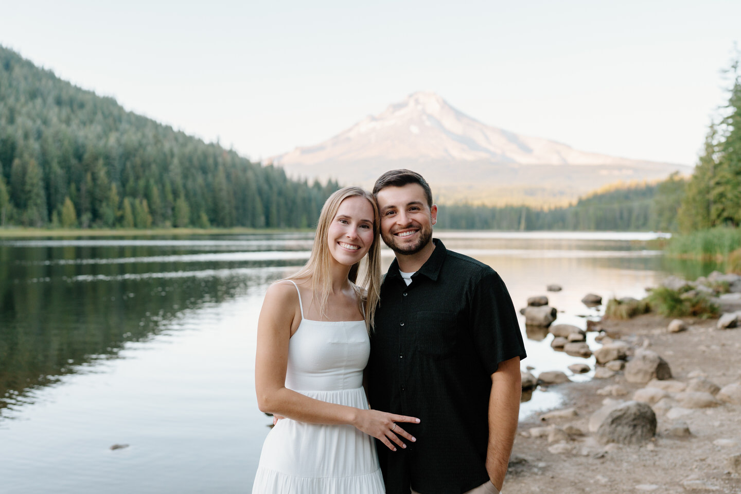 Smiling couple posing close together with the lake and forest framing them.