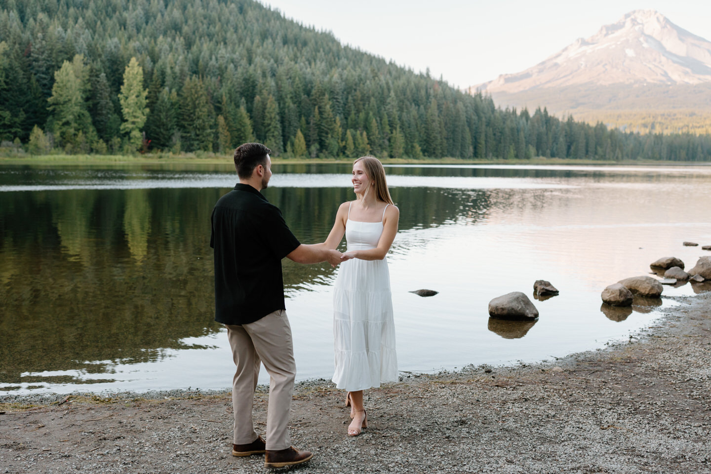 Couple standing across from each other near the shoreline with Mount Hood in the distance during engagement photos.