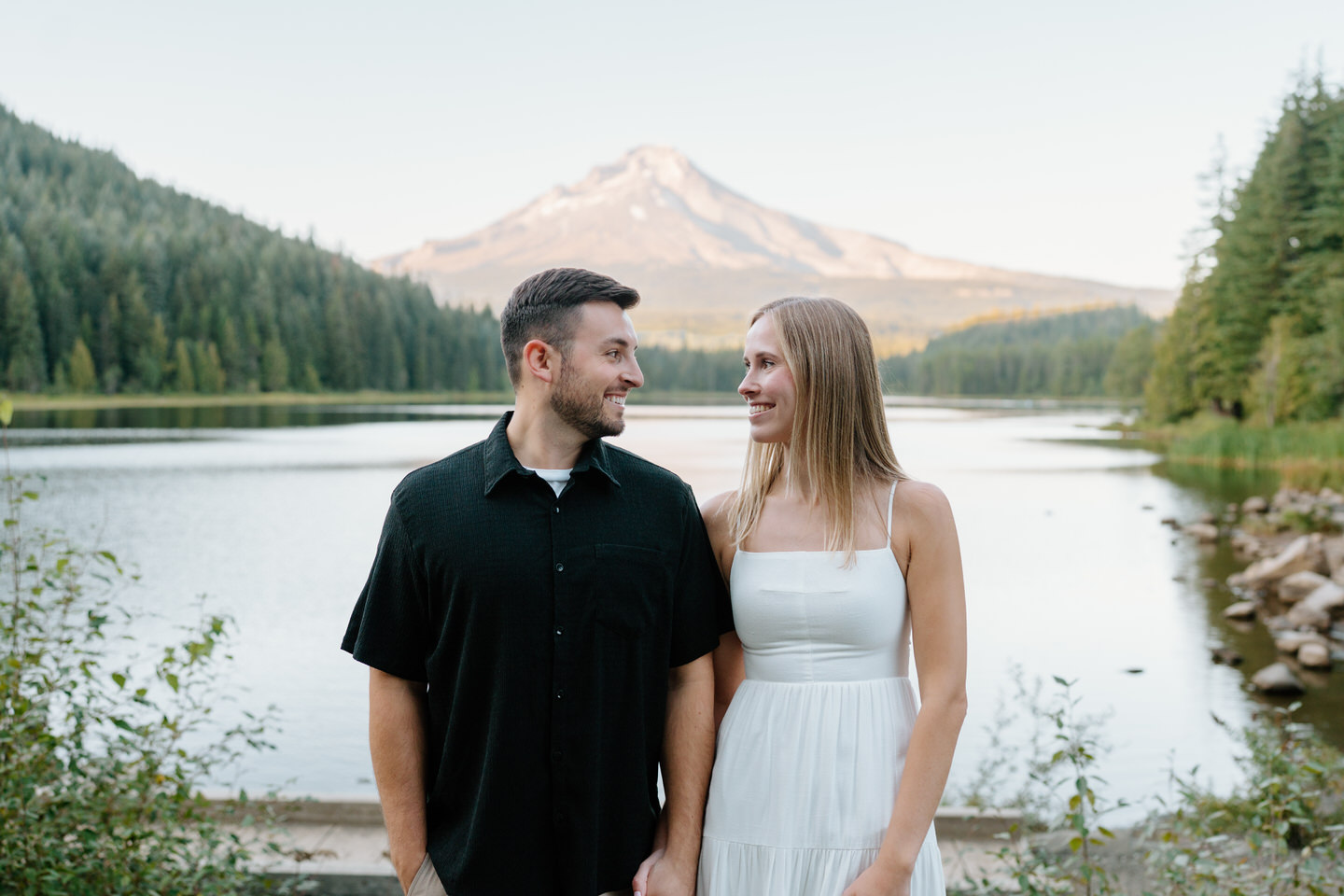 Couple walking side by side along the lakeshore with Mount Hood behind them during engagement photos at Trillium Lake.