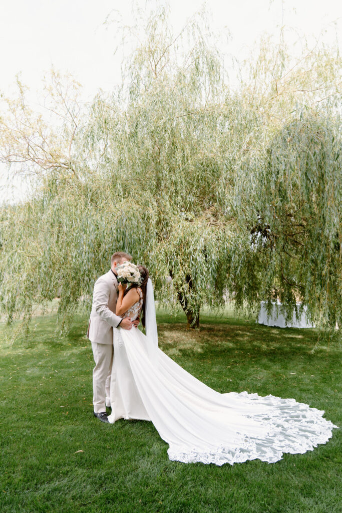 Couple kisses behind the bouquet at the willow tree.